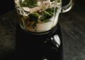 Batidora de vaso preparando un smoothie verde con frutas y verduras frescas en una cocina moderna