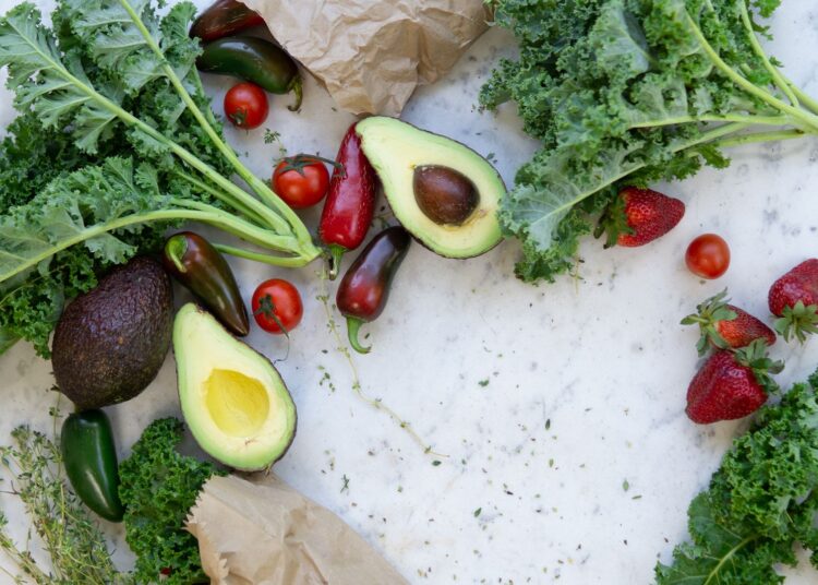Alimentos ricos en potasio: aguacates, verduras de hoja verde, tomates y frutas frescas sobre mesa