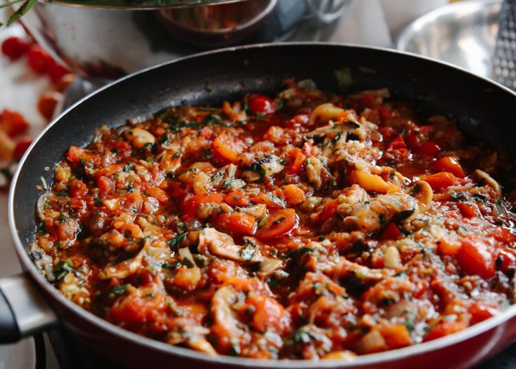 Pisto manchego cocinándose a fuego lento en una sartén con tomate, pimiento y calabacín