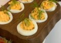 Bandeja con huevos rellenos de atún decorados con cebollino, listos para servir como aperitivo
