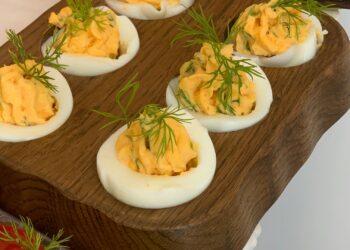 Bandeja con huevos rellenos de atún decorados con cebollino, listos para servir como aperitivo
