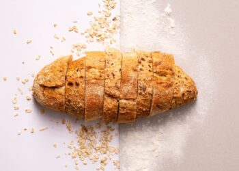 Pan de avena casero cortado en rebanadas sobre una superficie gris con copos de avena