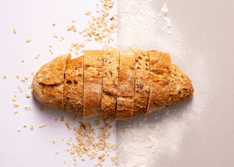 Pan de avena casero cortado en rebanadas sobre una superficie gris con copos de avena
