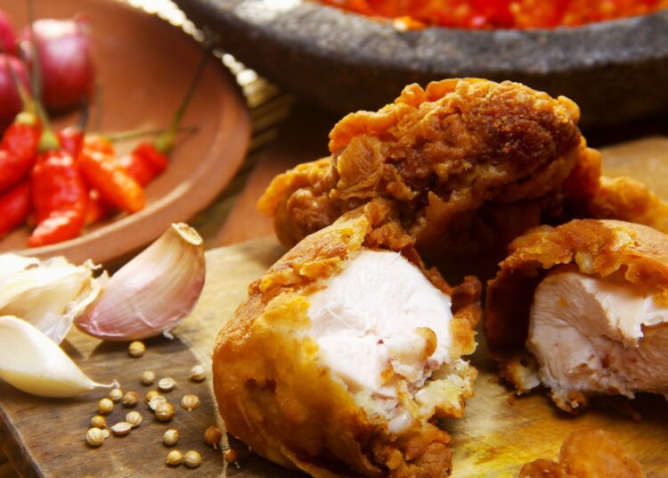 Pollo al ajillo troceado y dorado en sartén con dientes de ajo y perejil fresco