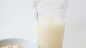 Leche de avena casera servida en un tarro de cristal junto a copos de avena sobre la mesa