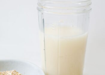 Leche de avena casera servida en un tarro de cristal junto a copos de avena sobre la mesa