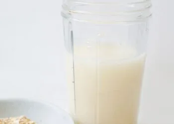Leche de avena casera servida en un tarro de cristal junto a copos de avena sobre la mesa