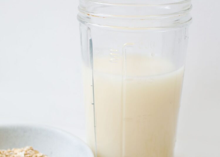 Leche de avena casera servida en un tarro de cristal junto a copos de avena sobre la mesa