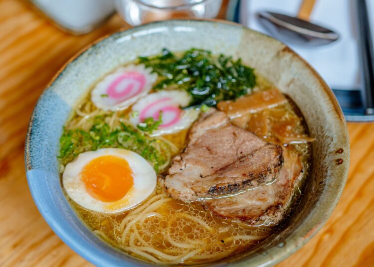 Bol de ramen casero con fideos, huevo, carne y cebolleta sobre mesa de madera