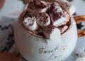 Taza de chocolate caliente casero cremoso sobre mesa de madera con hojas de otoño