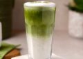 Vaso de matcha latte casero con hielo junto a un batidor de bambú y polvo de té matcha