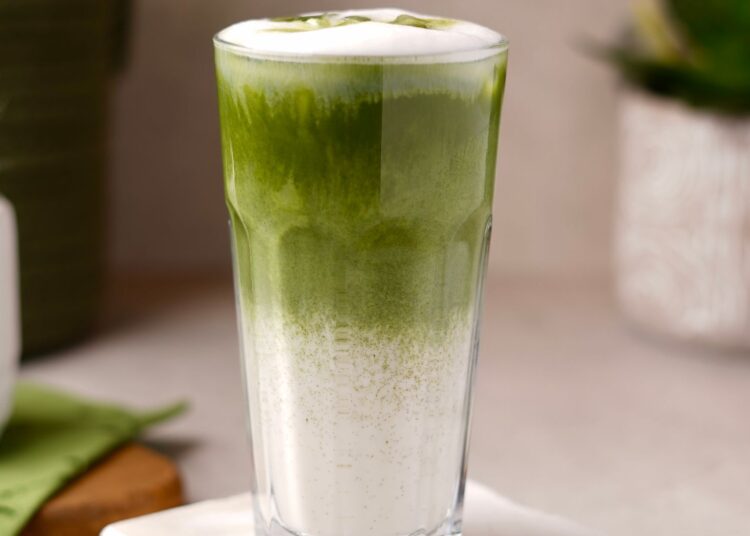 Vaso de matcha latte casero con hielo junto a un batidor de bambú y polvo de té matcha