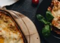 Lasaña de verduras recién horneada en fuente de cristal con queso gratinado y albahaca