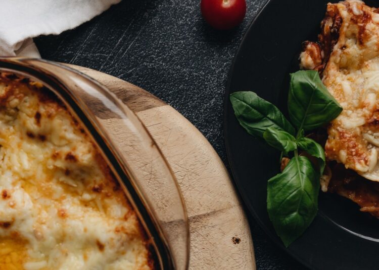 Lasaña de verduras recién horneada en fuente de cristal con queso gratinado y albahaca